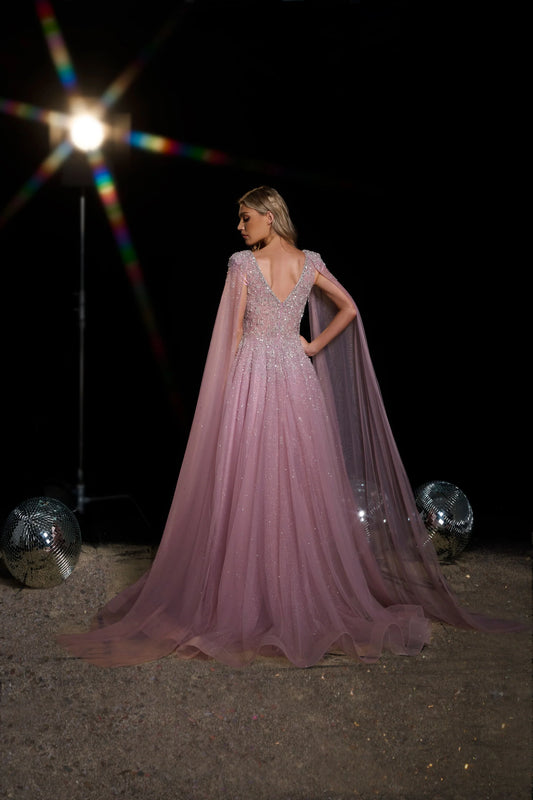 Woman in a pink evening gown with a cape against a dark background