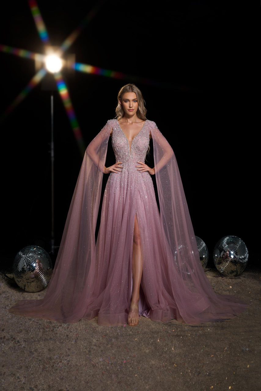 Woman in a glamorous pink evening gown with a high slit, standing against a dark background.