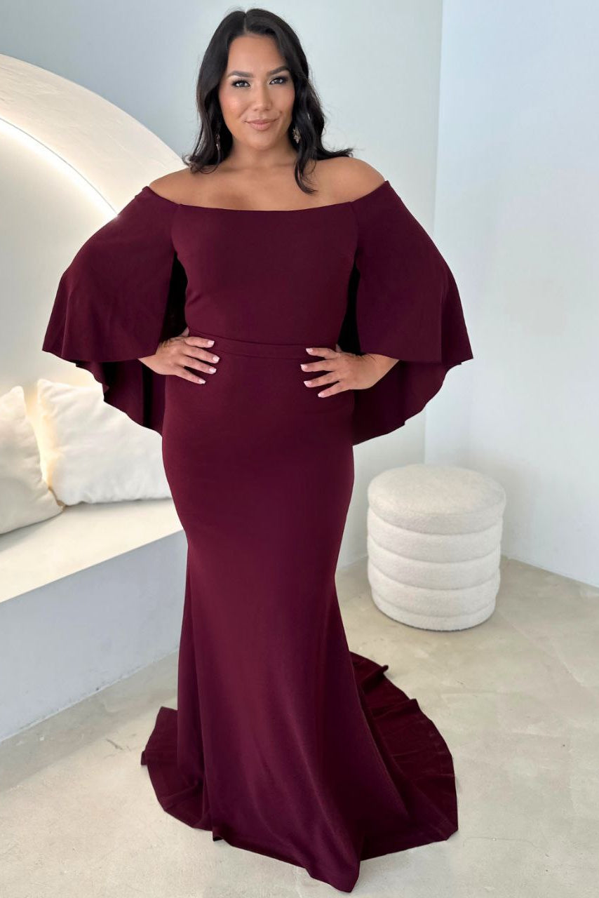 Woman wearing a burgundy off-shoulder gown in a modern interior setting