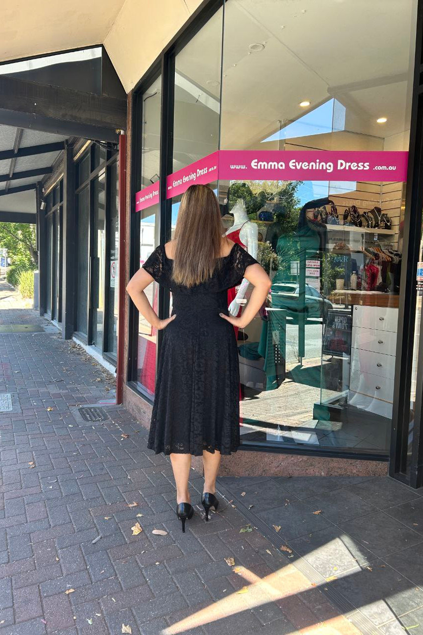 Woman in a black dress standing outside a store with a pink sign.