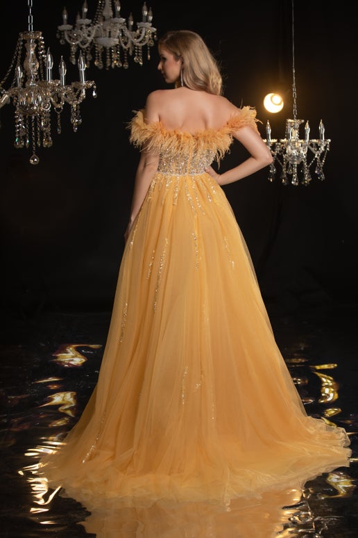 Woman in a yellow evening gown with feathered top in a glamorous setting with chandeliers.