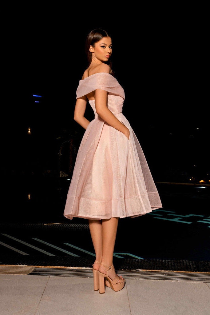 Woman in a pink off-shoulder dress standing by a pool at night.