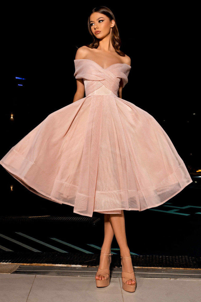 Woman in a pink off-shoulder dress standing on a street at night.