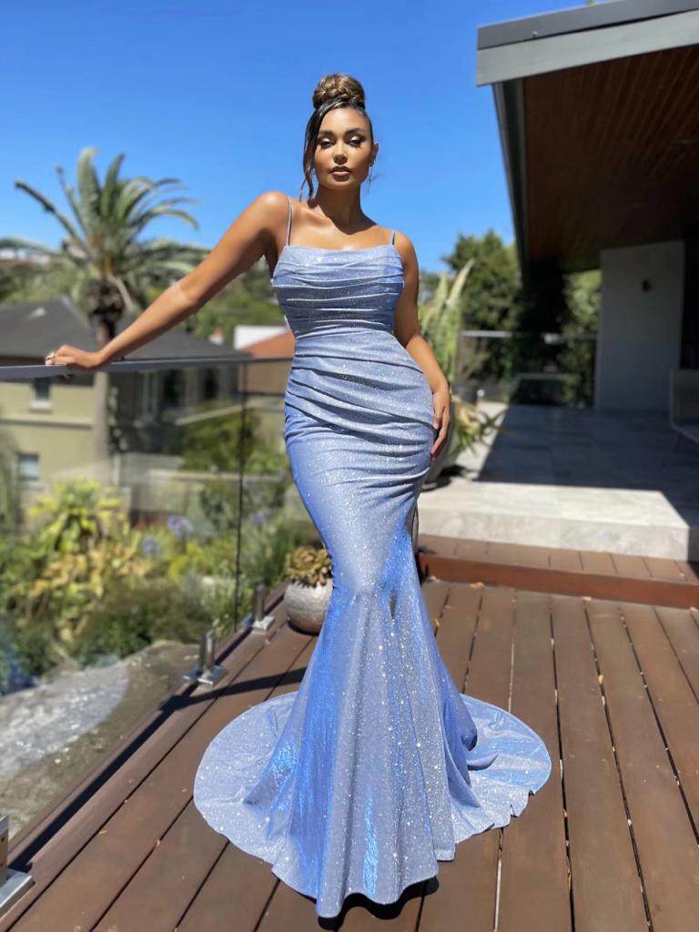Woman in a blue mermaid-style dress standing on a wooden deck with a garden background