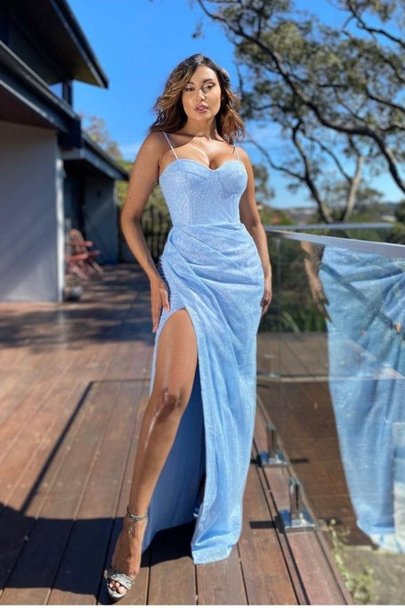 Woman in a light blue dress standing on a wooden deck with a clear sky background