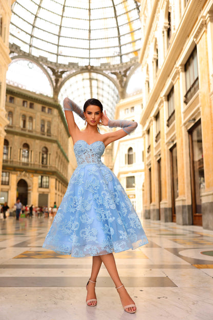 Woman in a light blue dress standing in an elegant indoor setting with architectural columns.