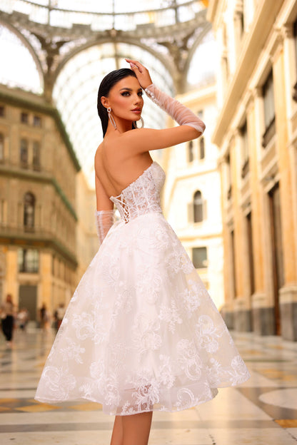 Woman in a white lace dress standing in an urban setting with architectural elements.