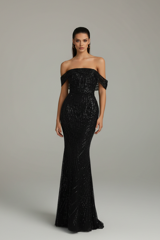 A woman modeling a floor-length off-the-shoulder black gown with a fitted silhouette and subtle shimmering texture, photographed against a plain light gray studio background.