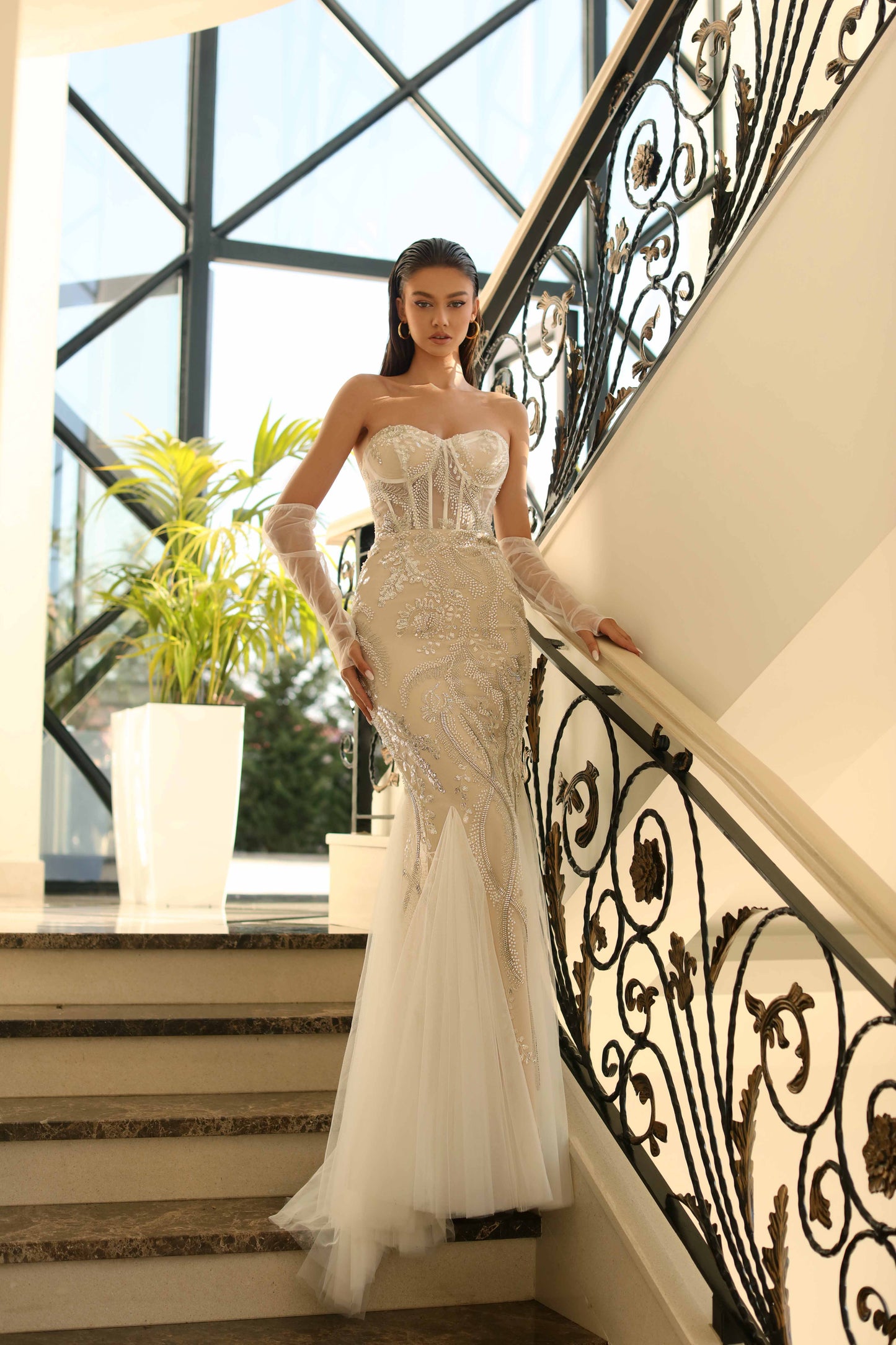 Woman in a white strapless gown standing on a staircase with decorative railings.