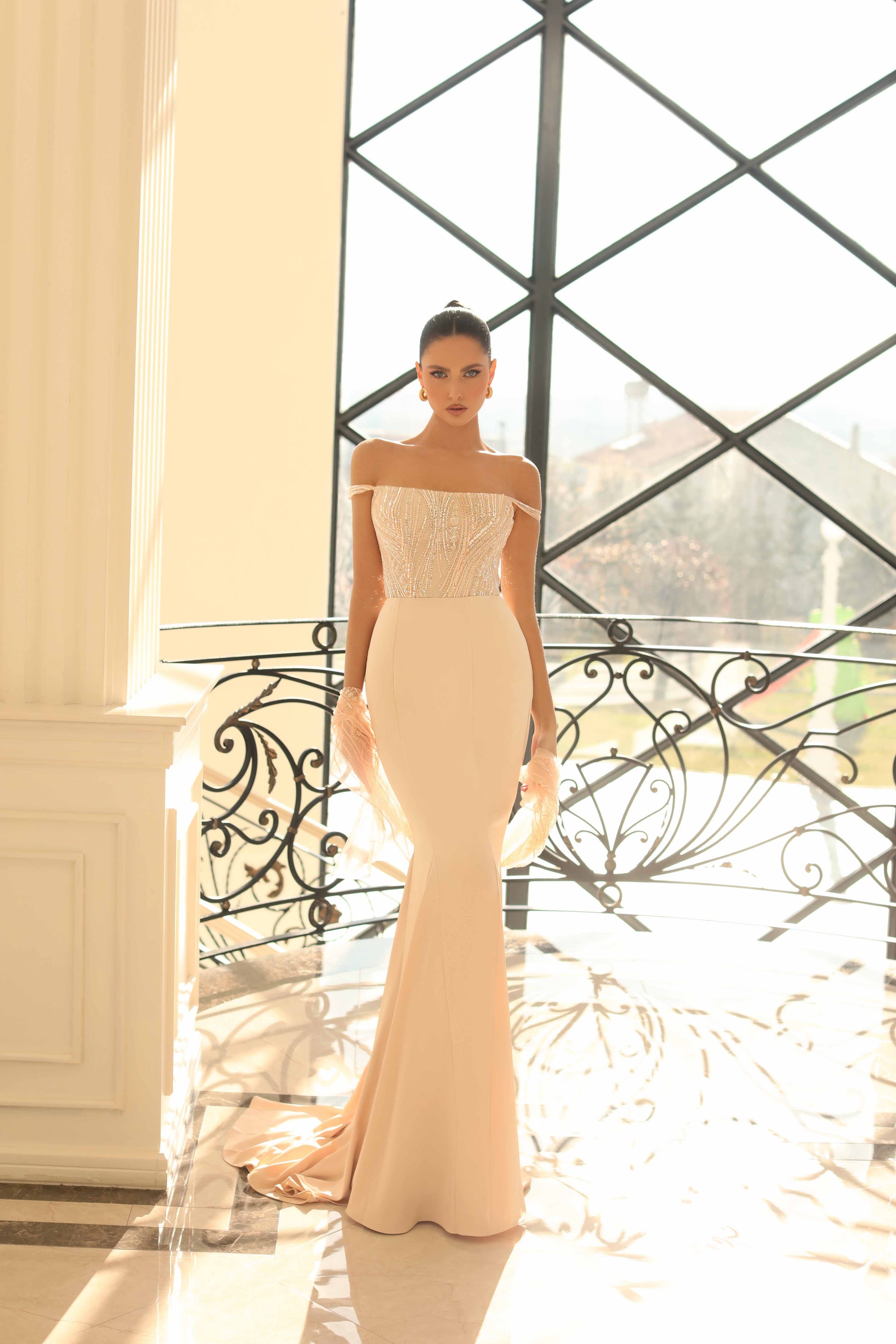 Woman in a beige off-shoulder gown standing in front of a decorative metal gate.