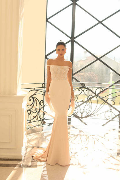 Woman in a beige off-shoulder gown standing in front of a decorative metal gate.