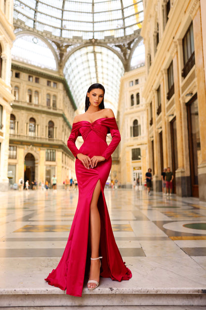 Woman in a red off-shoulder gown with a high slit standing in an elegant indoor setting.