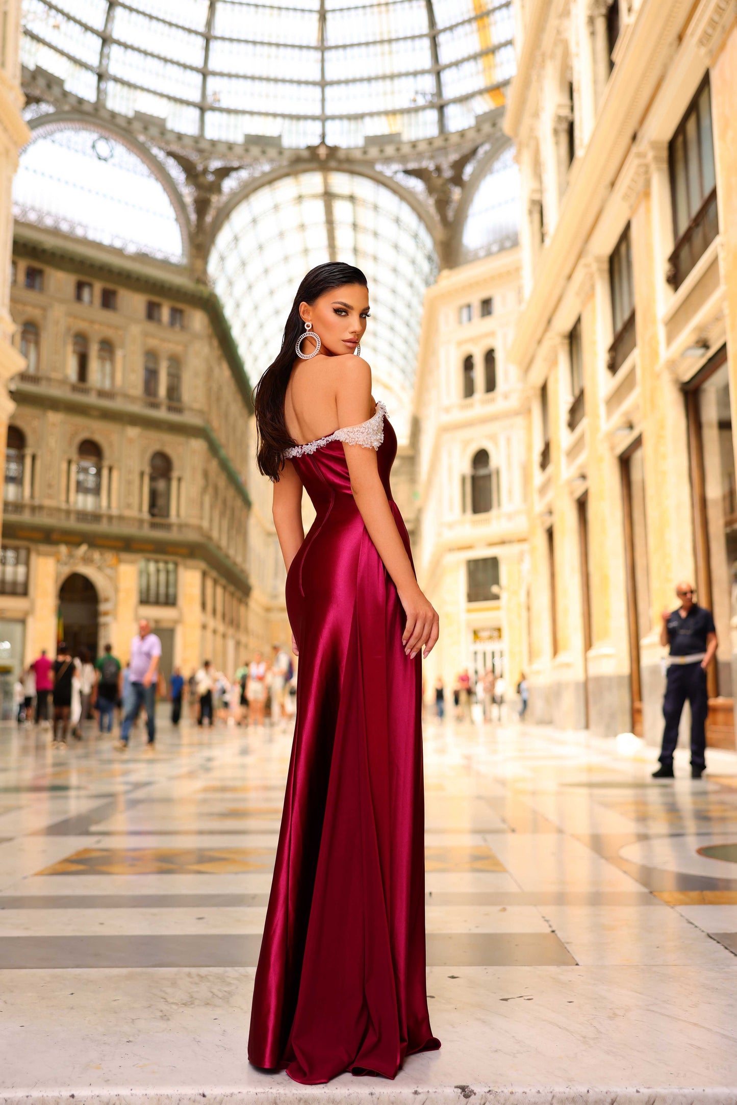 Woman in a burgundy evening gown standing in an elegant indoor setting with classical architecture.