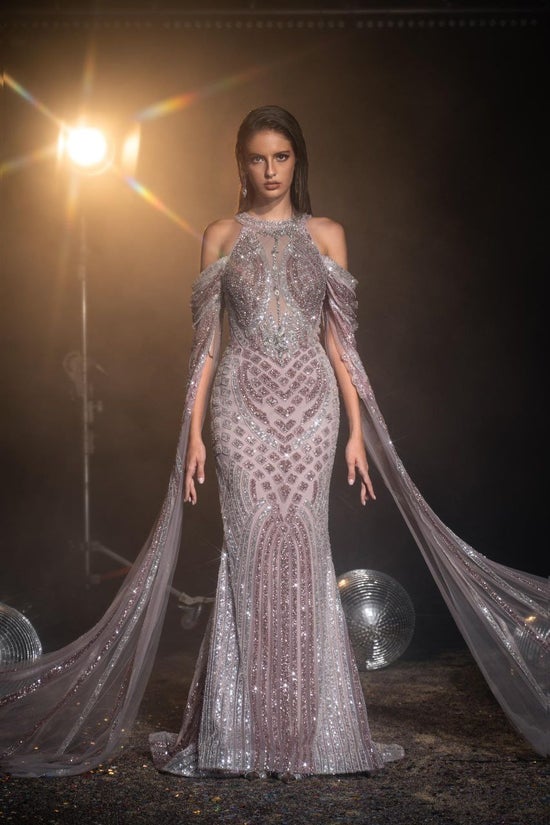 Model wearing a sparkling silver evening gown with a long train on a dark background