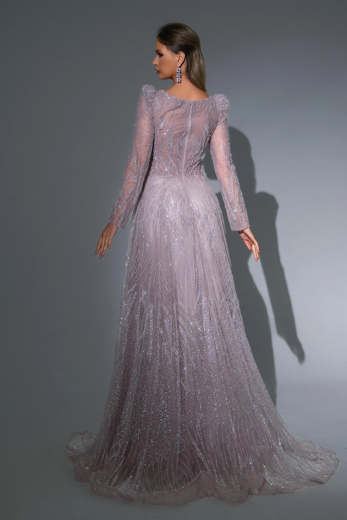 Woman wearing a long, elegant dress with sheer sleeves against a gray background