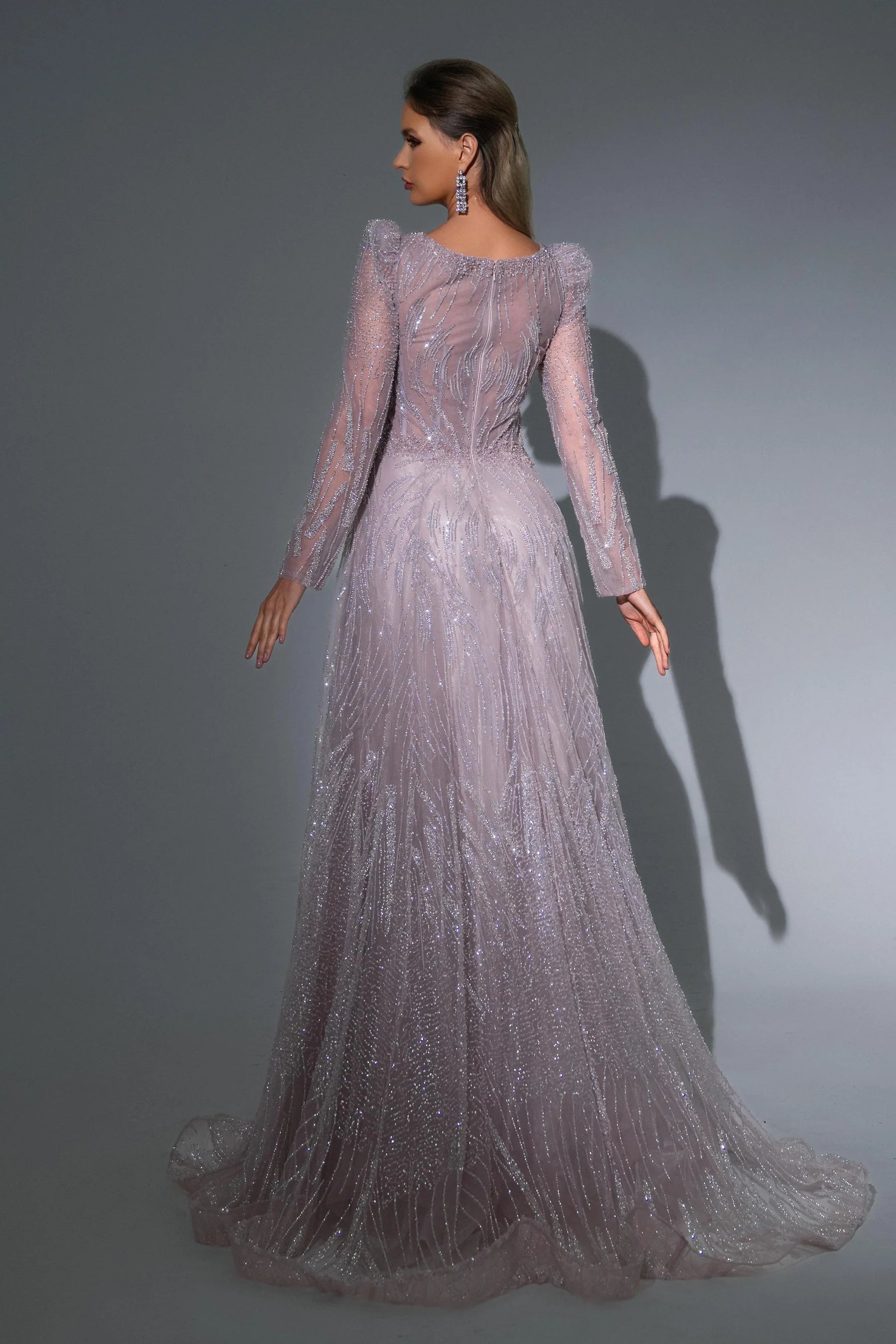 Woman wearing a long, elegant dress with sheer sleeves against a gray background