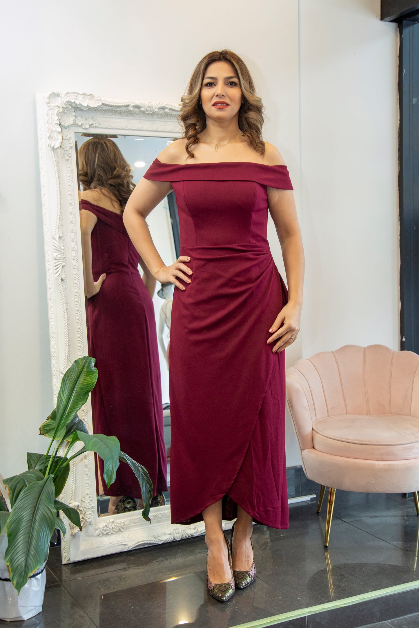 Woman in a burgundy off-shoulder dress standing in front of a mirror.