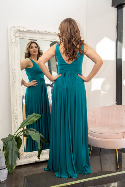 Woman in a teal dress standing in front of a mirror in a room with a pink chair and plant.