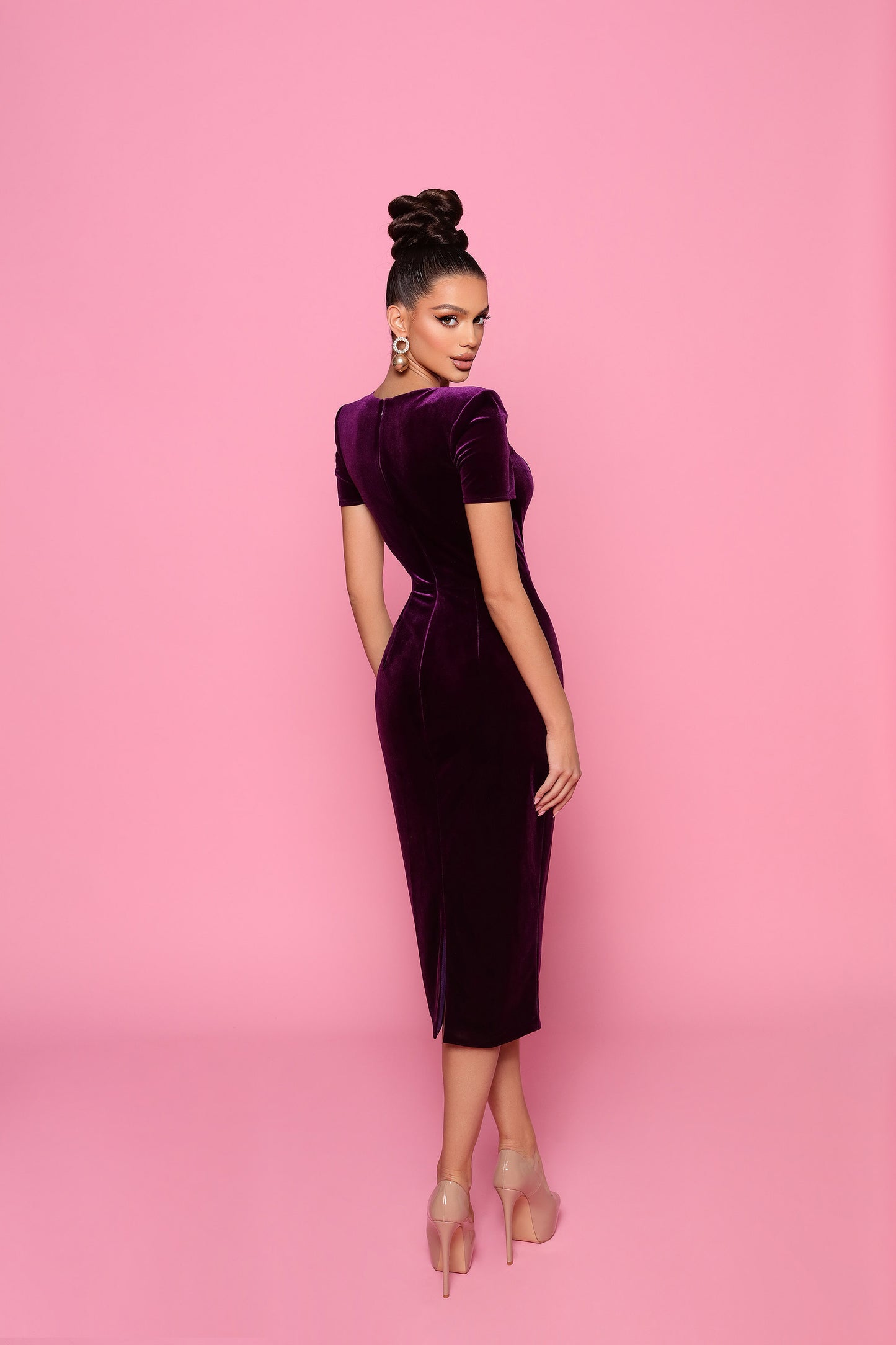 Woman wearing a purple velvet dress against a pink background