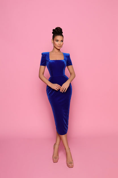 Woman wearing a blue velvet dress against a pink background