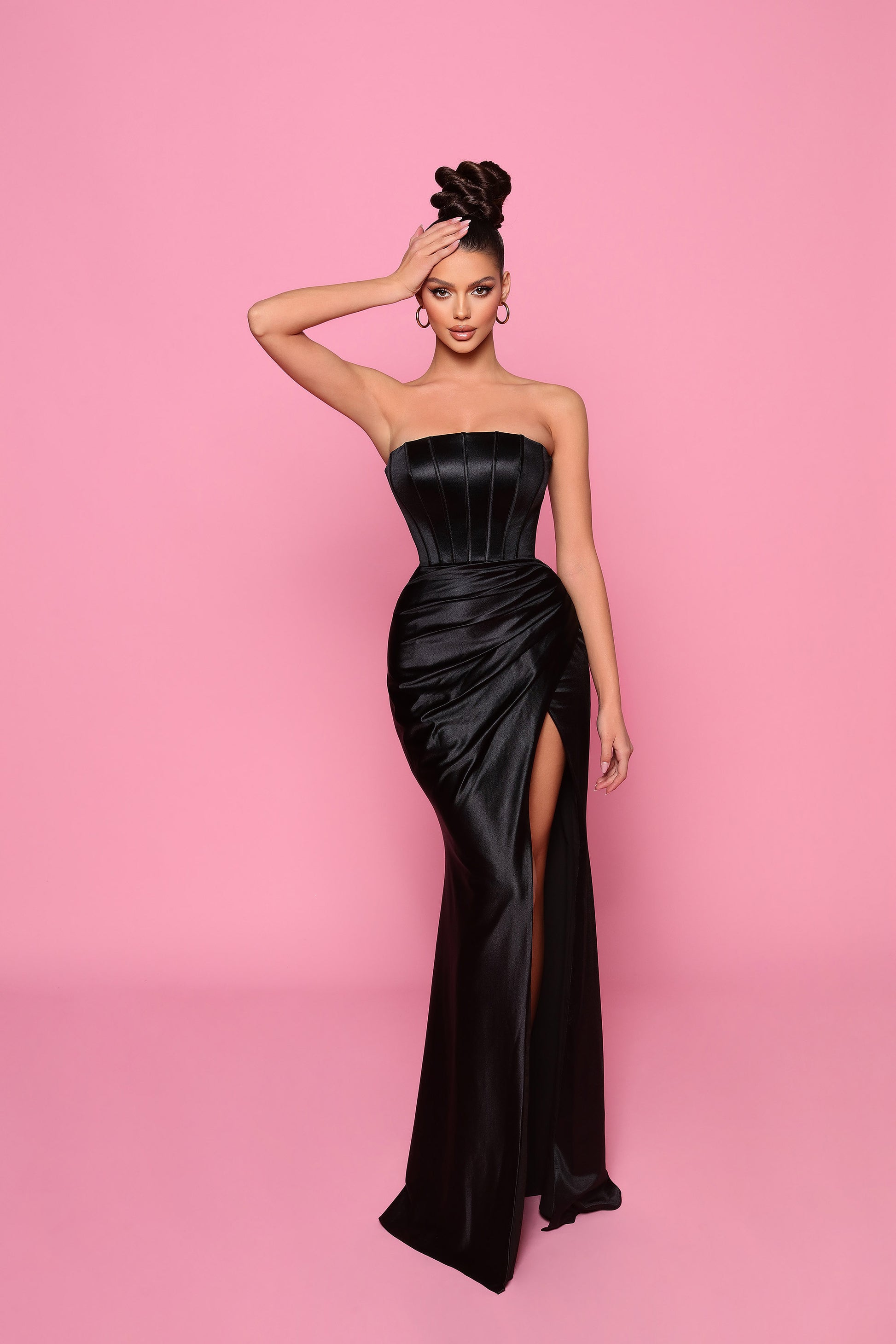 Woman in a black strapless gown with a high slit on a pink background