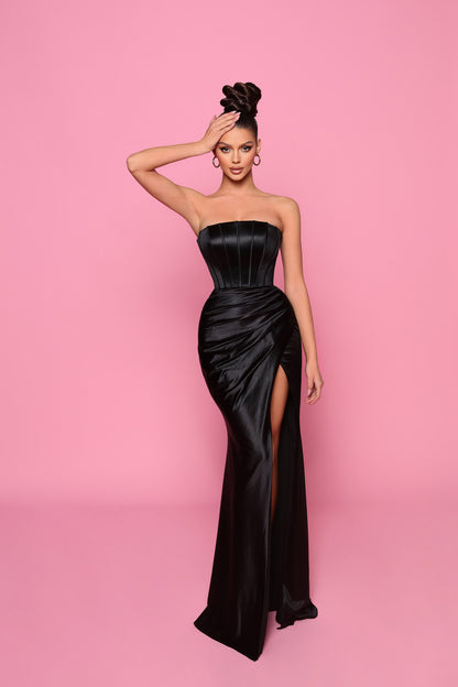 Woman in a black strapless gown with a high slit on a pink background