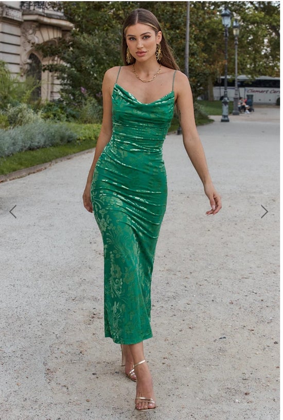 Woman in a green dress walking outdoors on a street.