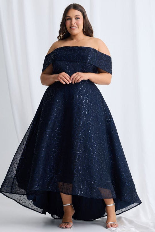 Woman wearing a navy off-shoulder lace dress against a white background