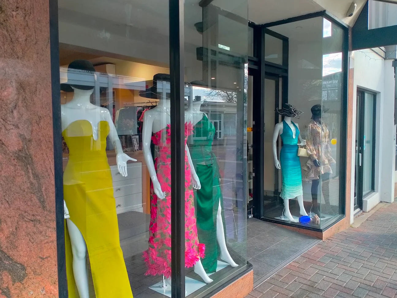 Mannequins wearing colorful dresses in a store window display.