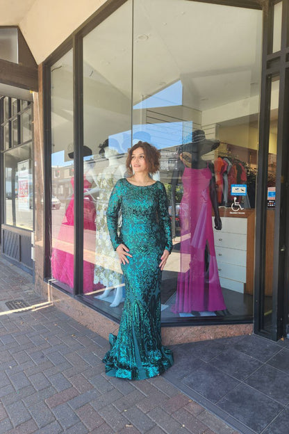 Woman in a teal evening gown standing outside a store with mannequins inside.