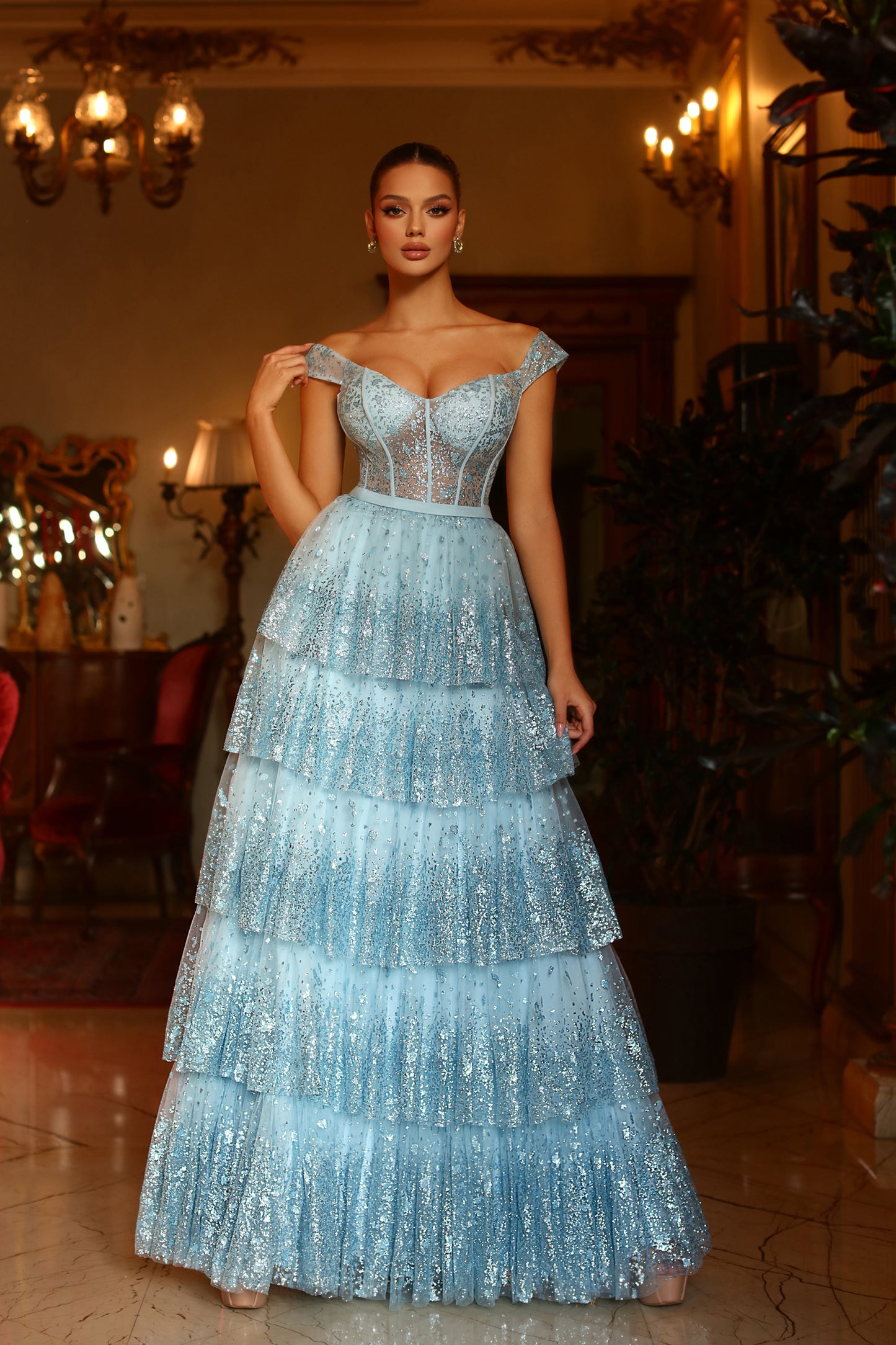 Woman in a light blue, tiered evening gown standing in an elegant indoor setting.