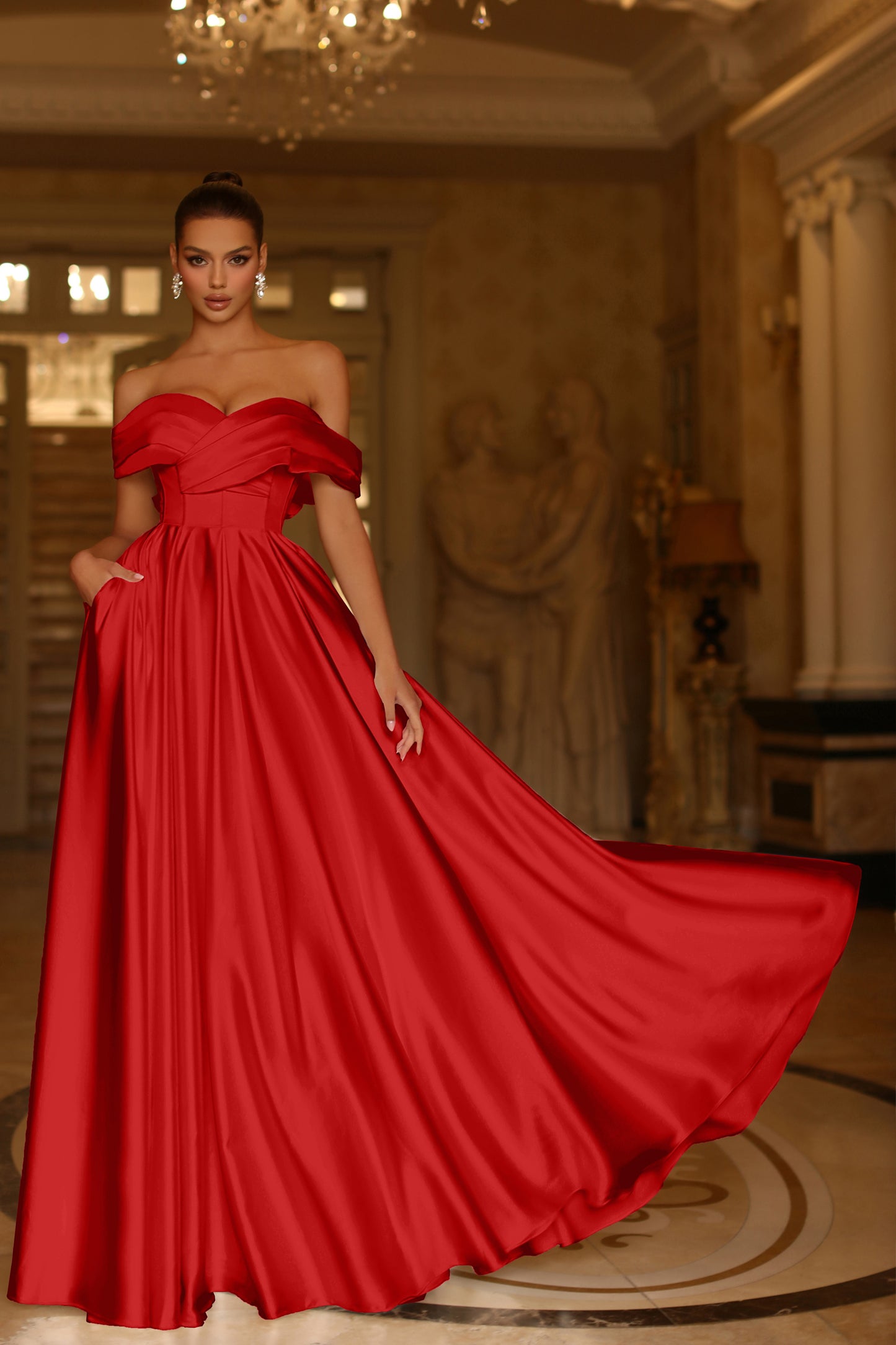 Woman in a red off-shoulder gown standing in an elegant room with chandelier.