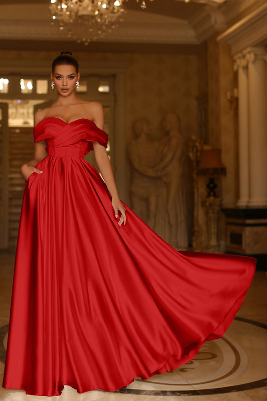Woman in a red off-shoulder gown standing in an elegant room with chandelier.