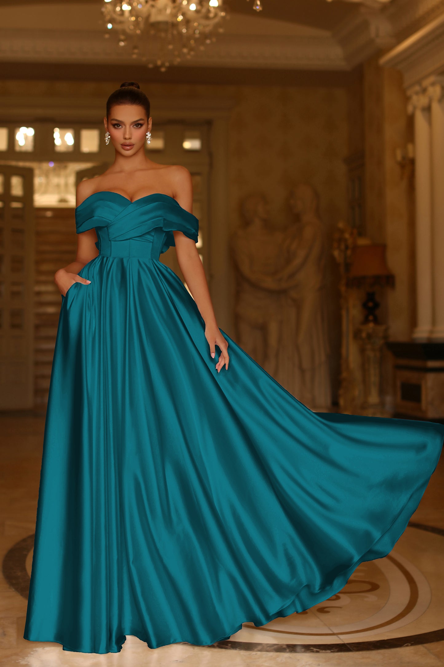 Woman in a teal evening gown standing in an elegant room with chandeliers.