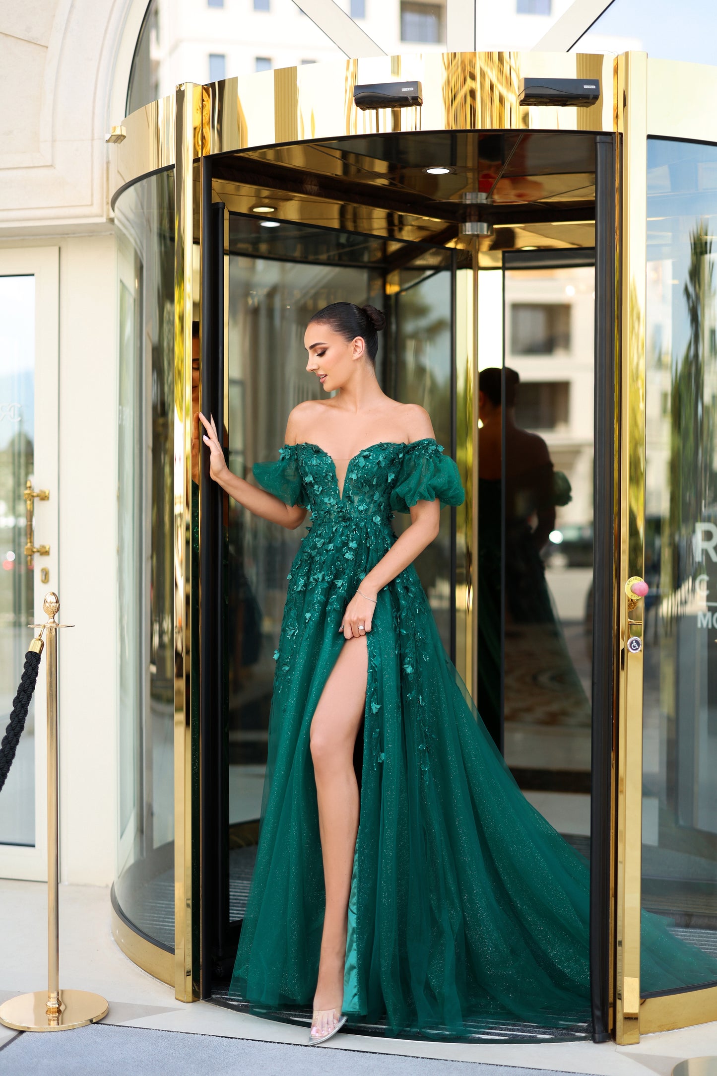 Woman in a green evening gown exiting a gold revolving door.