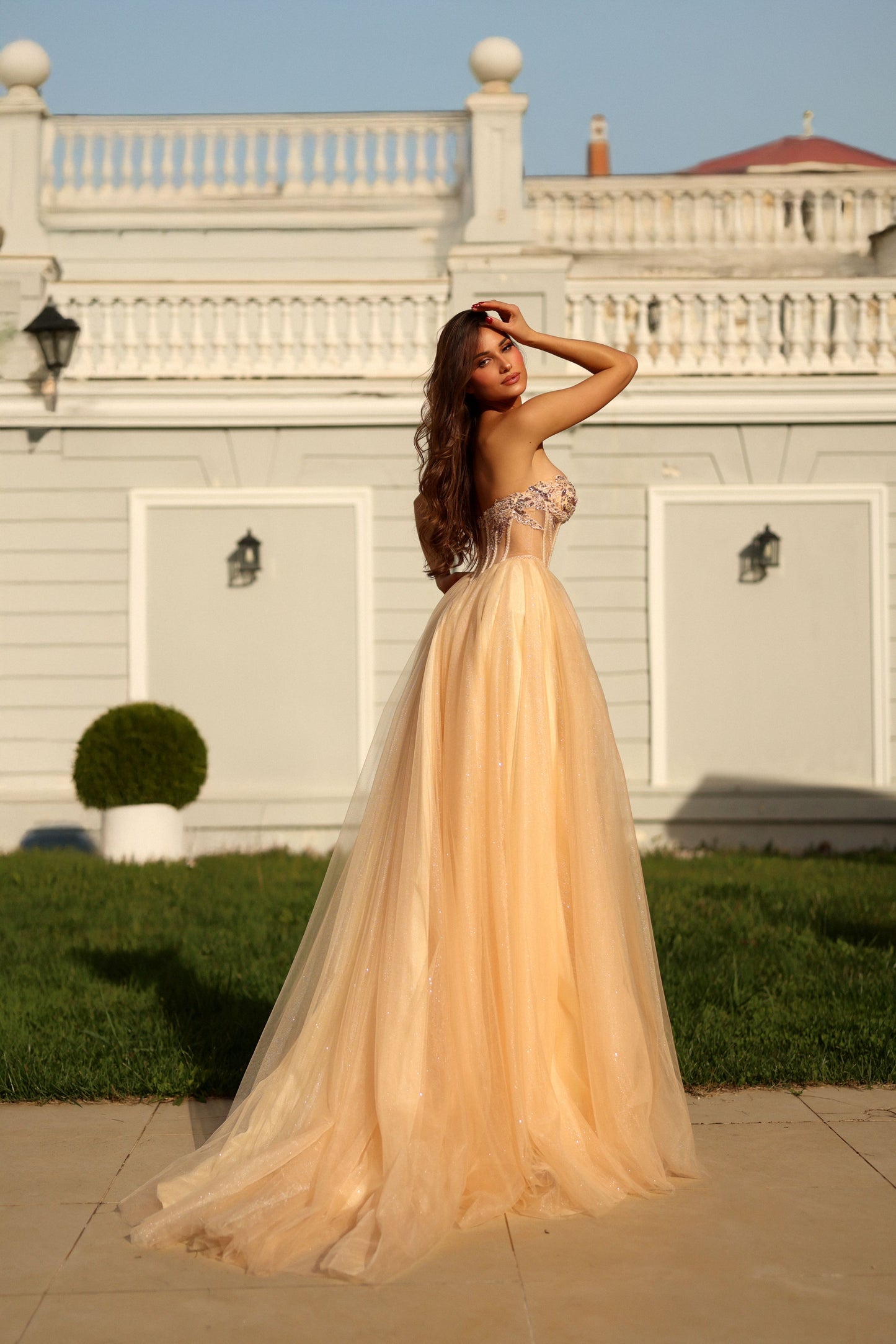 Woman in a peach evening gown standing in front of a white building with columns.