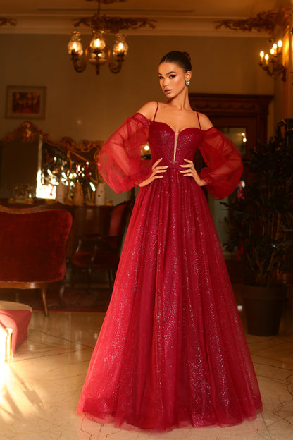 Woman in a red evening gown standing in an elegant room with chandeliers.