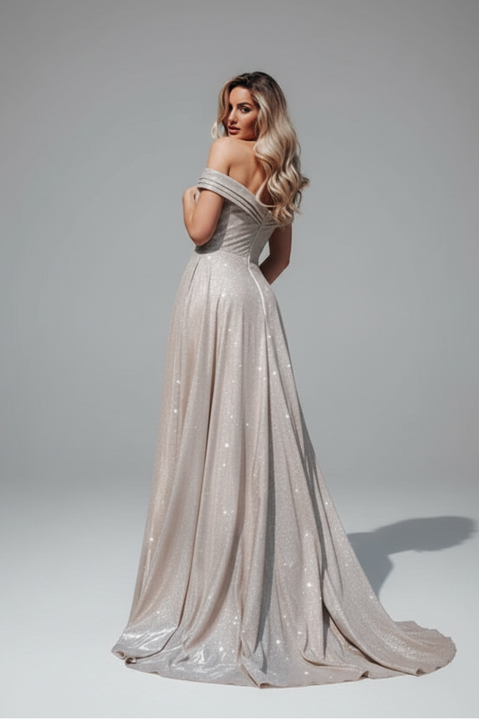 A woman modeling a floor-length off-the-shoulder evening gown in a shimmering champagne-beige color with subtle sequin details, photographed against a neutral gray studio backdrop.