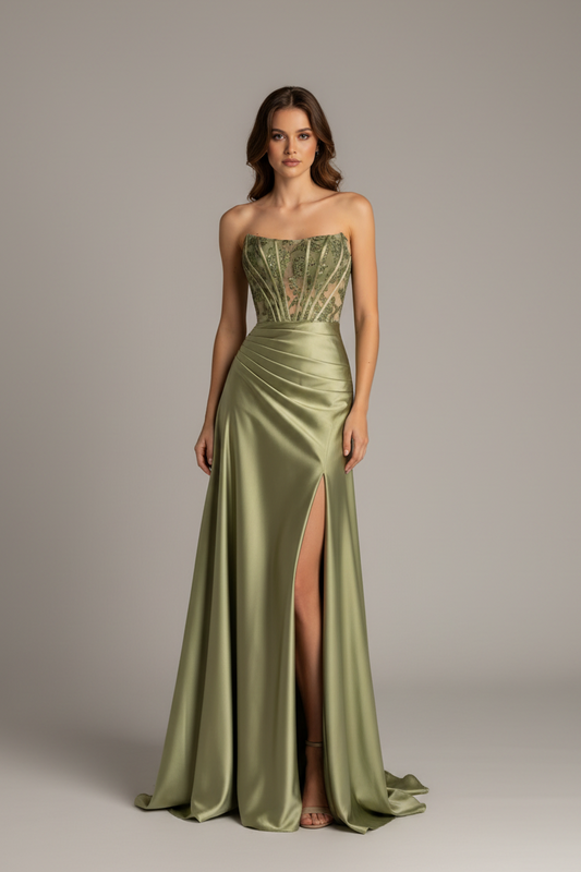 A woman models a strapless floor-length gown in a muted sage green satin fabric with a fitted bodice, ruched waist, and high front slit, photographed against a plain light gray studio background.
