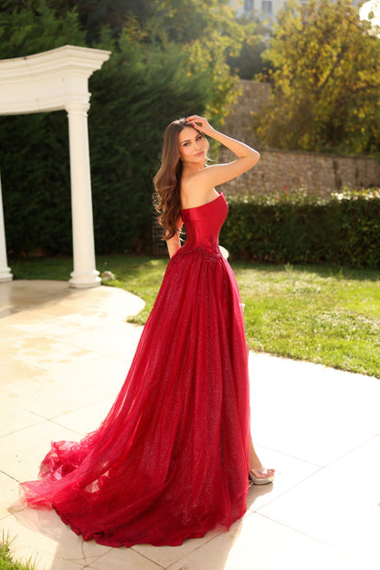 Woman in a red dress standing outdoors with greenery in the background