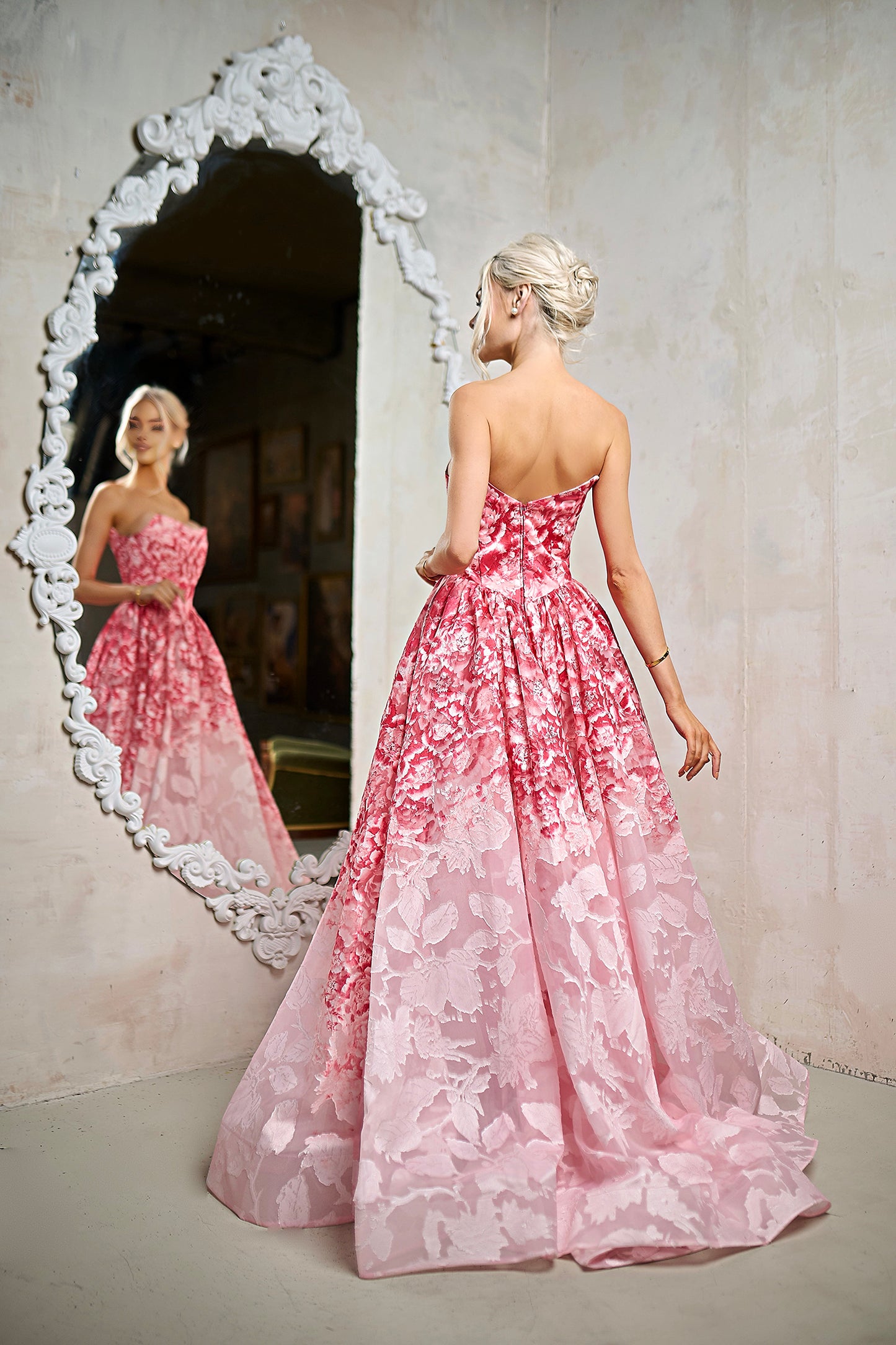 Woman in a pink floral dress standing in front of a decorative mirror.