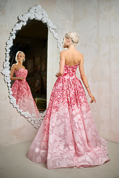 Woman in a pink floral dress standing in front of a decorative mirror.