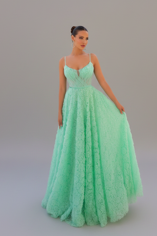 A woman modeling a mint green formal gown with a lace bodice and a voluminous tulle skirt, standing against a neutral gray studio background.
