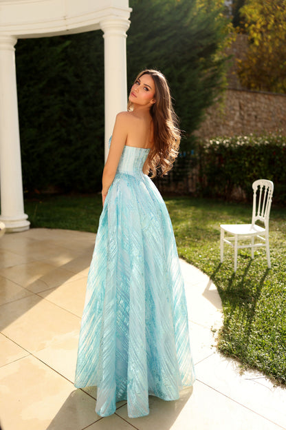 Woman in a light blue strapless gown standing outdoors near a white columned structure.