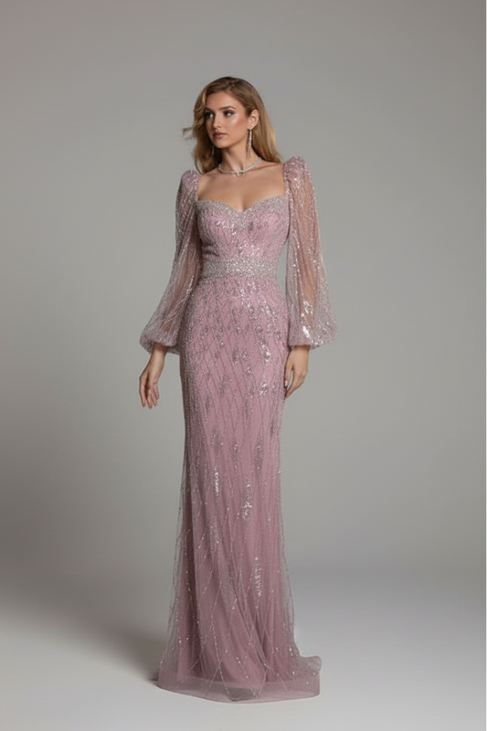 Woman in a pink evening gown with sheer sleeves standing in a dimly lit room with chandeliers.