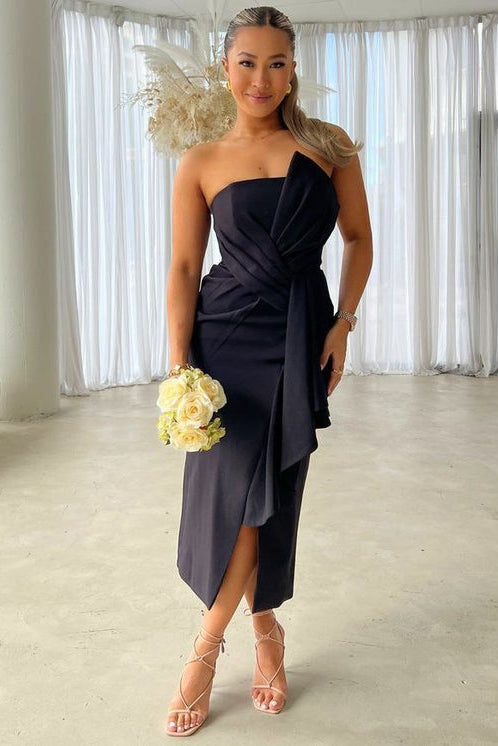 Woman in a black one-shoulder dress holding flowers indoors.