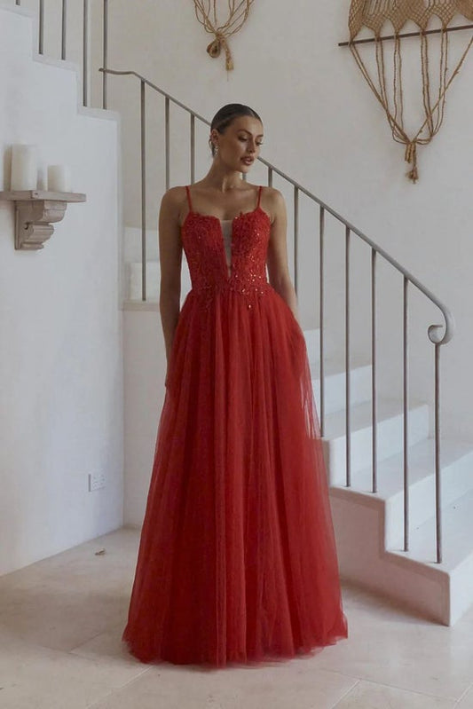Woman in a red evening gown standing in a staircase interior.