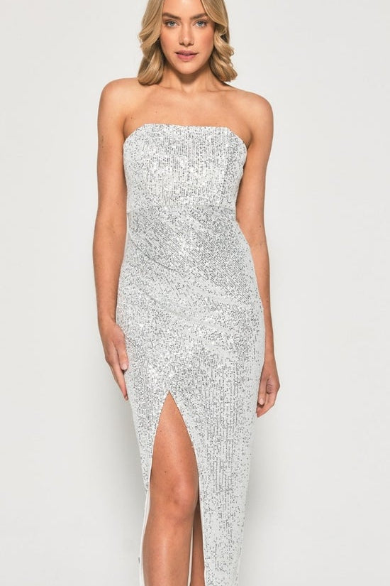 Woman wearing a strapless, sequined dress with a high slit on a plain background